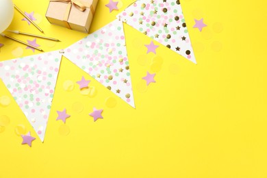 Confetti, garland, candles and gift box on yellow background, flat lay. Space for text