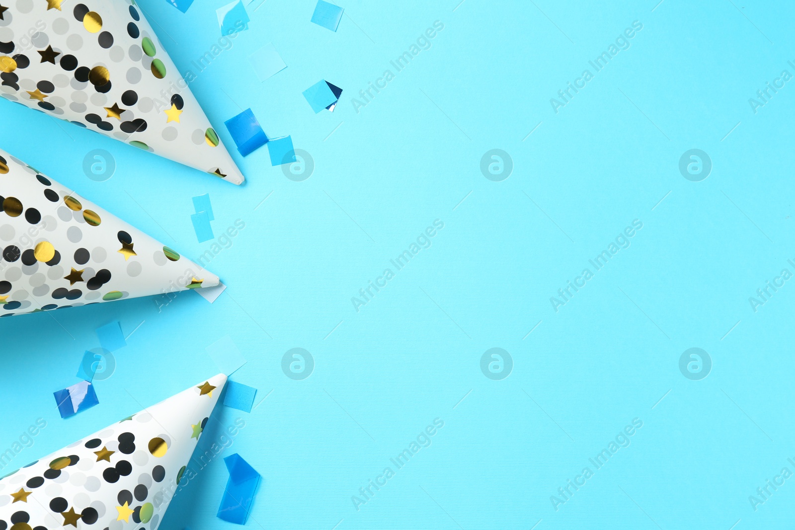 Photo of Party hats and confetti on light blue background, flat lay. Space for text