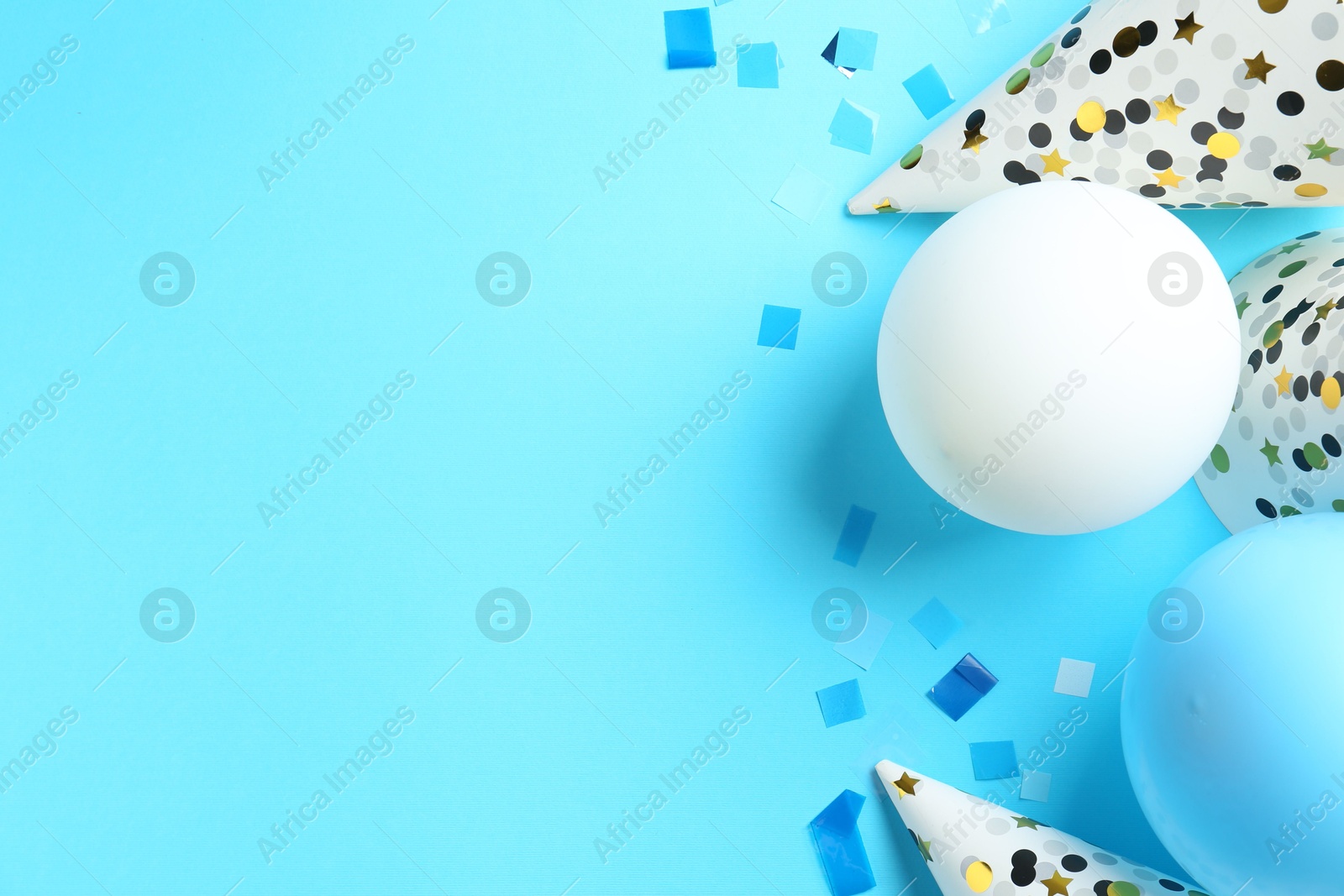 Photo of Party hats, air balloons and confetti on light blue background, flat lay. Space for text