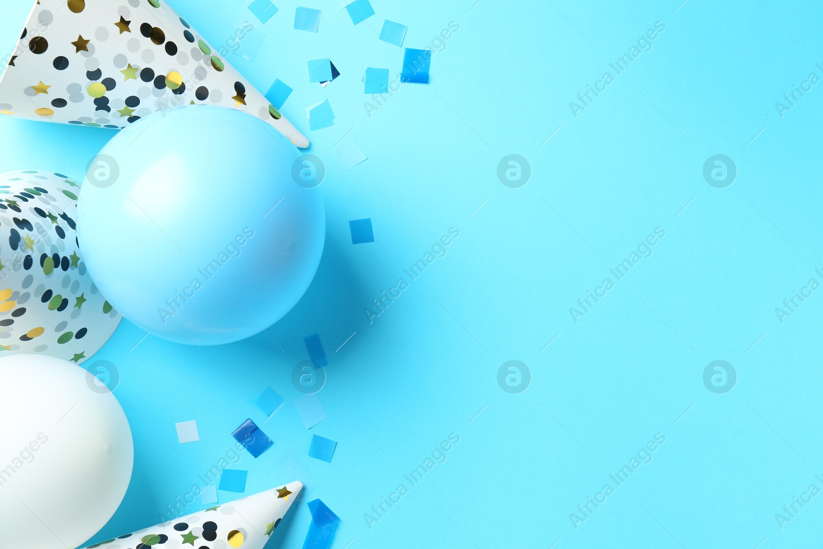 Photo of Party hats, air balloons and confetti on light blue background, flat lay. Space for text