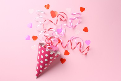 Party hat with confetti and streamers on pink background, flat lay