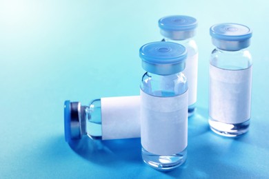 Medication in glass vials with blank labels on light blue background, space for text