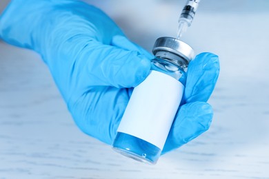 Nurse filling syringe with medication from vial at white wooden table, closeup