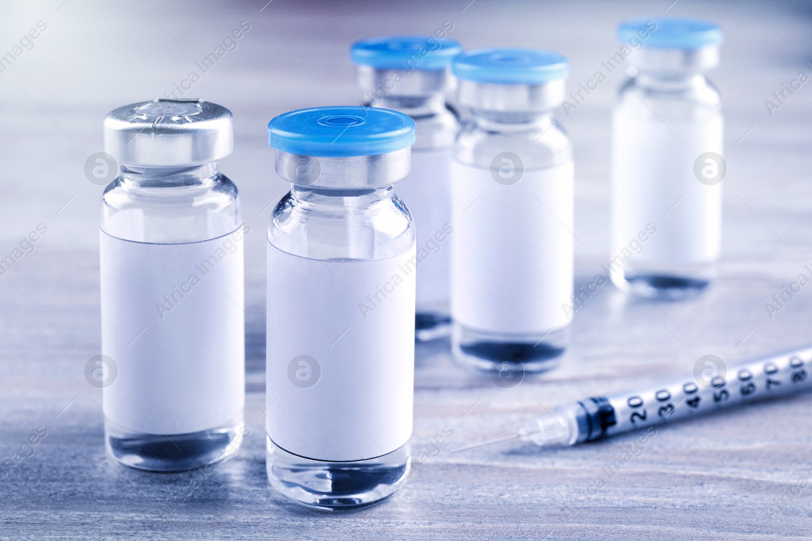 Image of Medication in glass vials with blank labels and syringe on wooden table, closeup