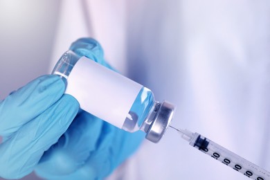 Nurse filling syringe with medication from glass vial, closeup