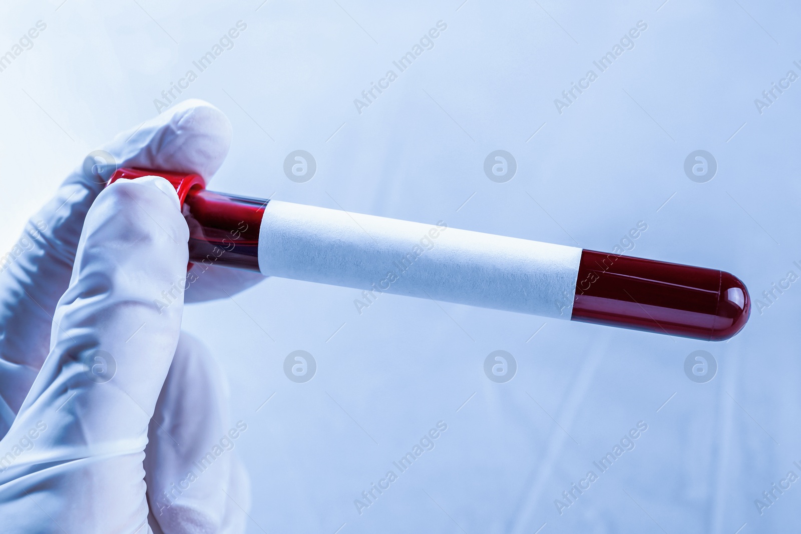 Image of Laboratory worker holding test tube with blood sample and blank label on blurred background, closeup. Medical analysis