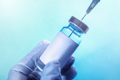 Nurse filling syringe with medication from vial on light blue background, closeup