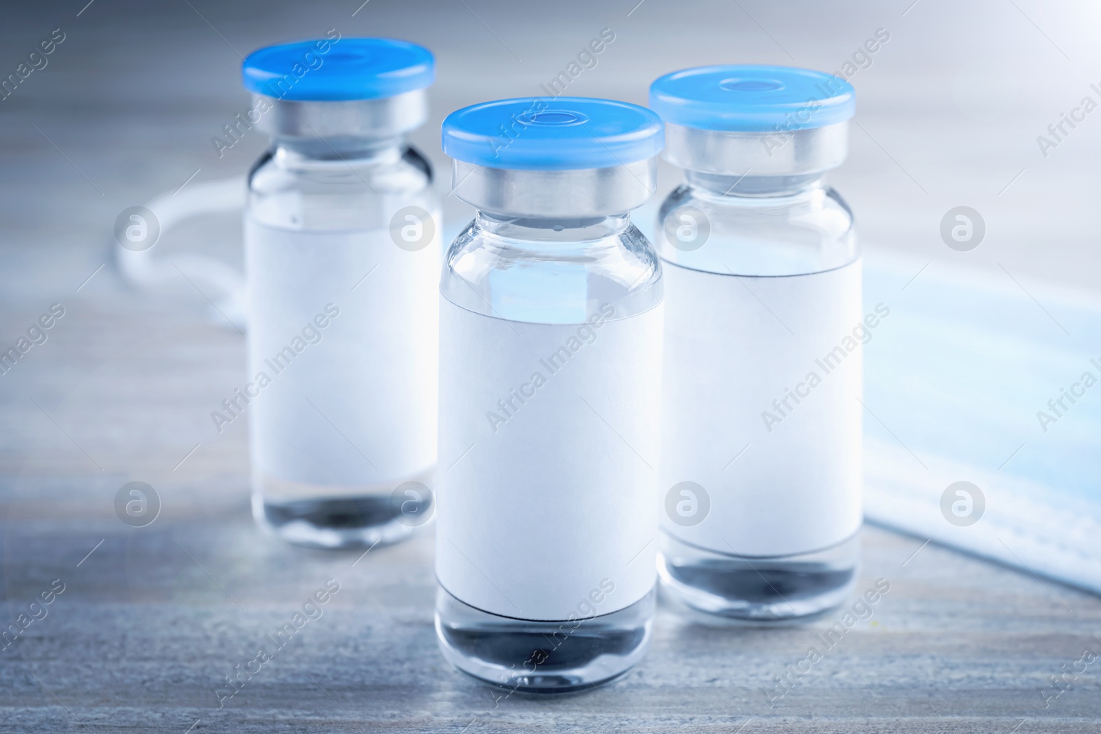 Image of Medication in glass vials and medical mask on wooden table, closeup