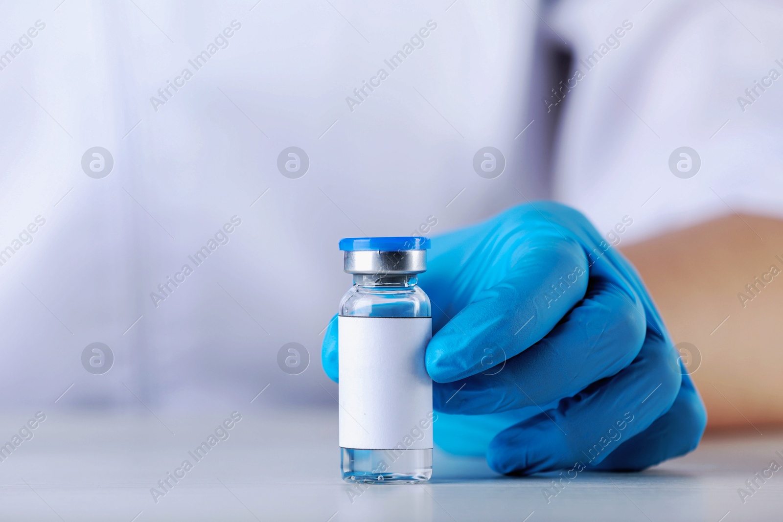 Image of Nurse with glass vial of medication at table, closeup