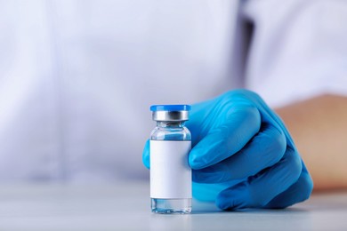 Image of Nurse with glass vial of medication at table, closeup