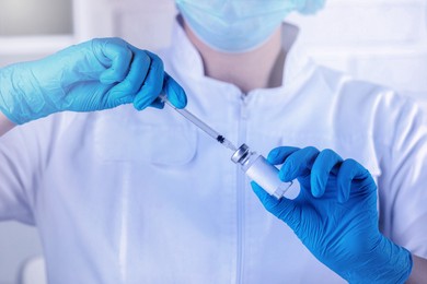 Nurse filling syringe with medication from glass vial in hospital, closeup