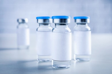 Medication in glass vials with blank labels on white wooden table