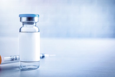 Image of Medication in glass vial with blank label and syringe on white wooden table, space for text