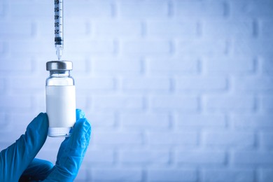 Nurse filling syringe with medication from vial near white brick wall, closeup. Space for text