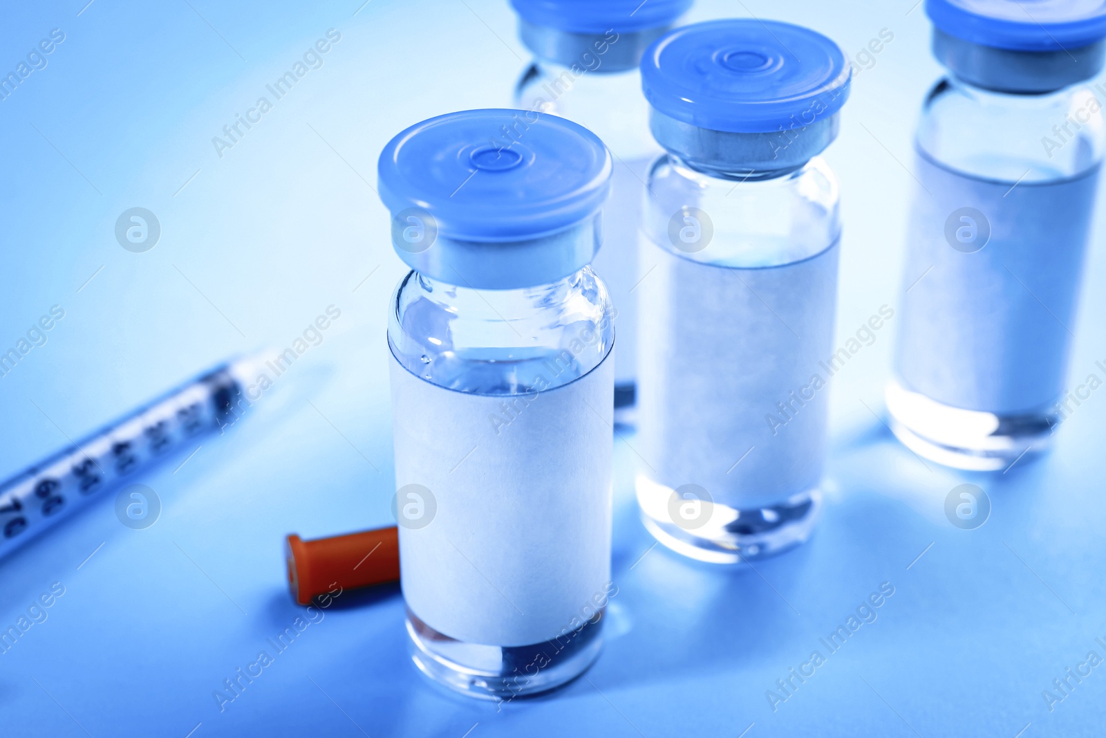 Image of Medication in glass vials and syringe on light blue background, closeup