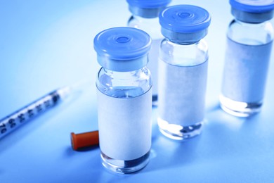 Image of Medication in glass vials and syringe on light blue background, closeup