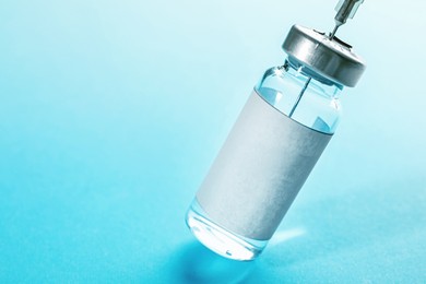 Image of Filling syringe with medication from vial on turquoise background, closeup. Space for text