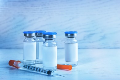 Medication in glass vials and syringe on white wooden table, space for text