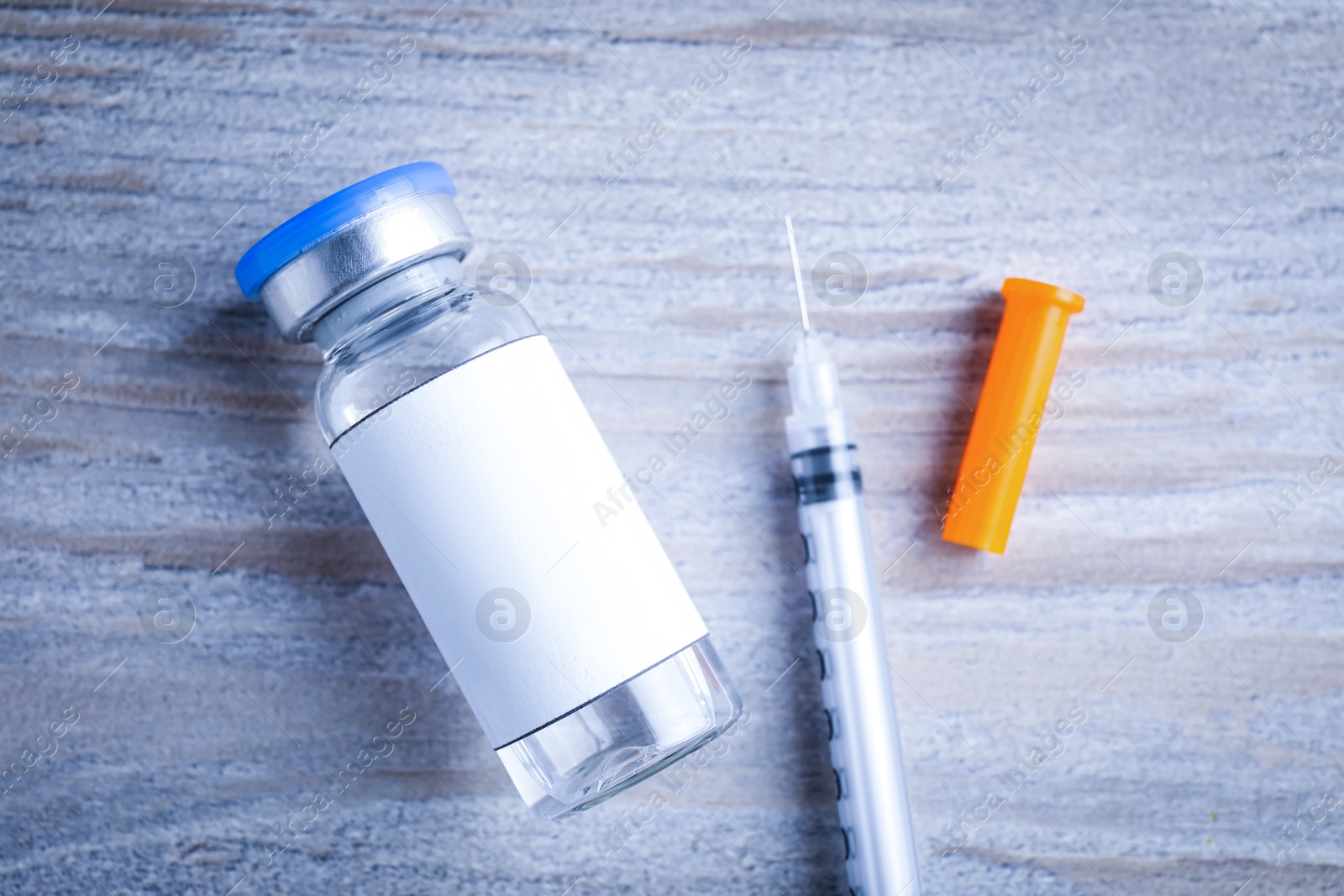 Image of Medication in glass vial with blank label and syringe on wooden table, flat lay