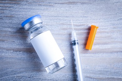 Medication in glass vial with blank label and syringe on wooden table, flat lay