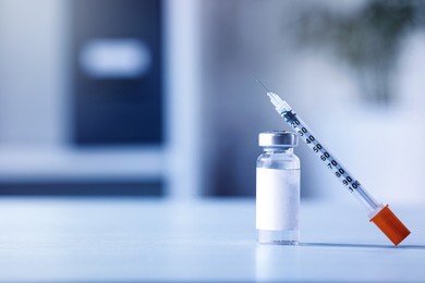 Medication in glass vial and syringe on white table, space for text