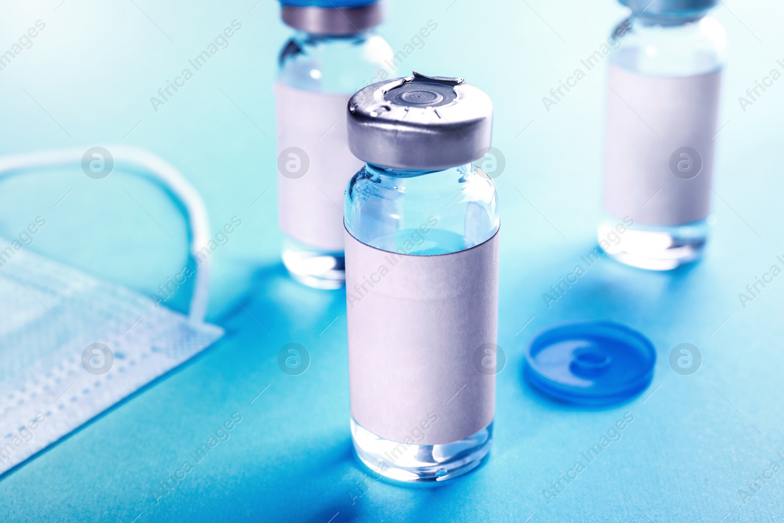 Image of Medication in glass vials and medical mask on light blue background, closeup