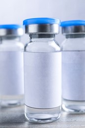 Image of Medication in glass vials with blank labels on wooden table, closeup