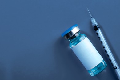 Image of Medication in glass vial and syringe on dark blue background, flat lay. Space for text