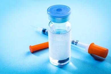 Image of Medication in glass vial and syringe on light blue background, closeup. Space for text