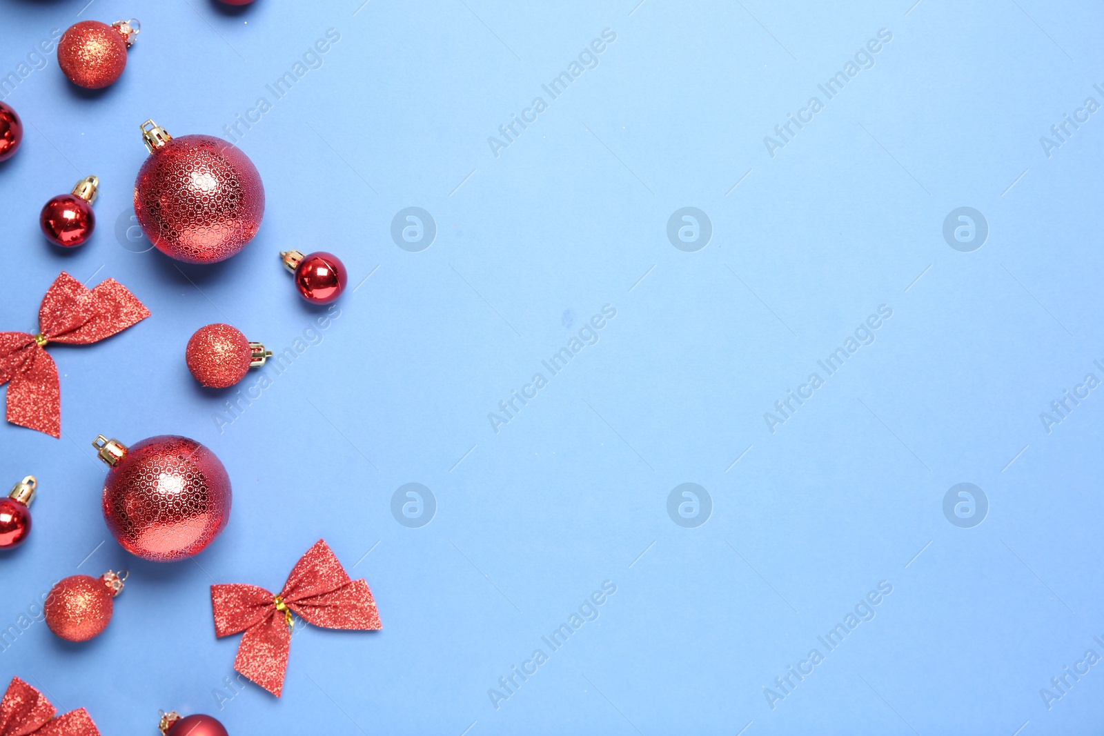 Photo of Christmas balls and bows on light blue background, flat lay. Space for text