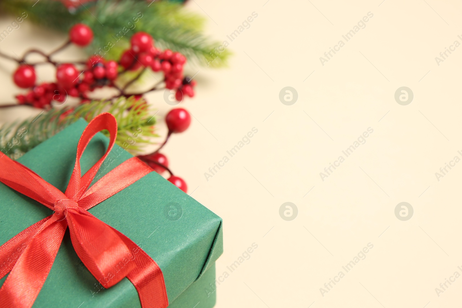 Photo of Christmas gift box, berries and fir tree branches on beige background, closeup. Space for text