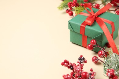 Photo of Christmas gift box, berries and fir tree branches on beige background, closeup. Space for text