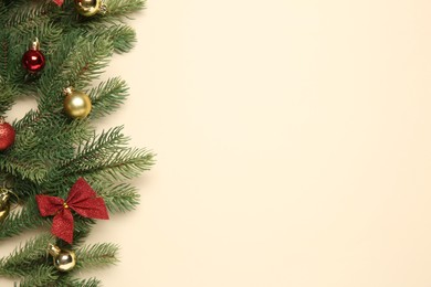 Photo of Fir tree branches with Christmas balls and bow on beige background, flat lay. Space for text