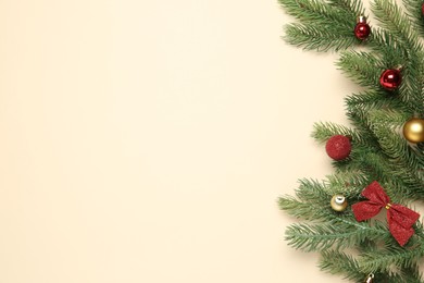 Photo of Fir tree branches with Christmas balls and bow on beige background, flat lay. Space for text