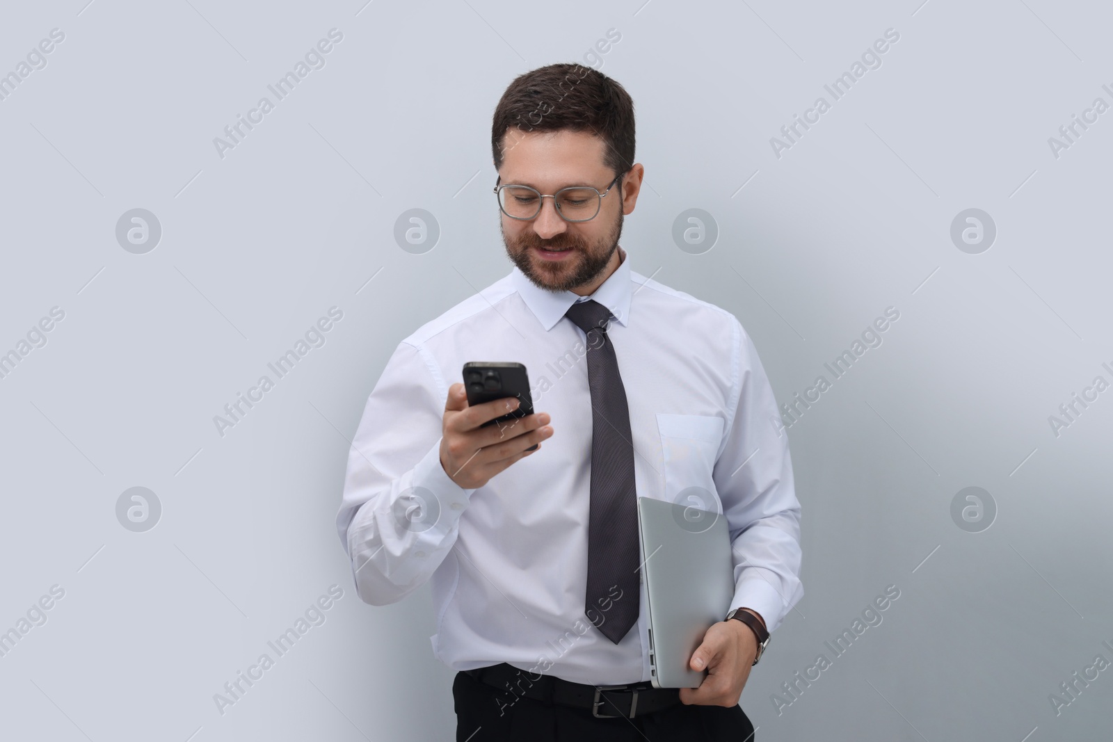 Photo of Portrait of businessman with laptop using smartphone on grey background