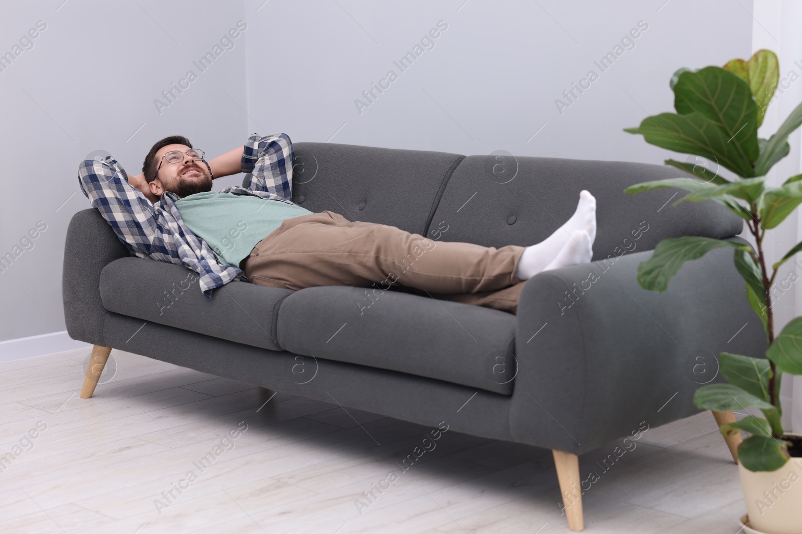 Photo of Smiling man with hands behind his head relaxing on sofa at home