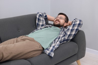 Photo of Smiling man with hands behind his head relaxing on sofa at home