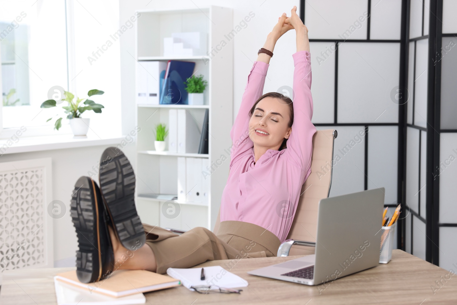 Photo of Smiling businesswoman holding legs on table in office. Break time