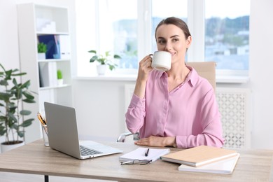 Smiling businesswoman drinking coffee at table in office. Break time