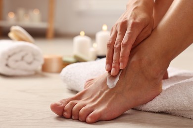 Photo of Woman applying moisturizing cream onto her feet on floor, closeup. Body care