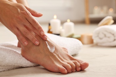 Photo of Woman applying moisturizing cream onto her feet on floor, closeup. Body care