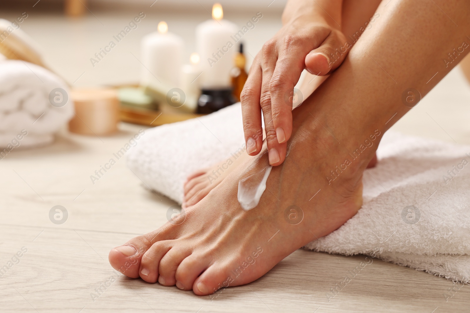 Photo of Woman applying moisturizing cream onto her feet on floor, closeup. Body care