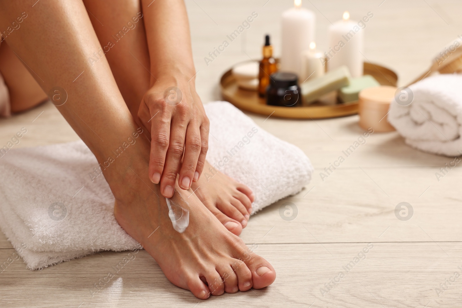 Photo of Woman applying moisturizing cream onto her feet on floor, closeup. Body care