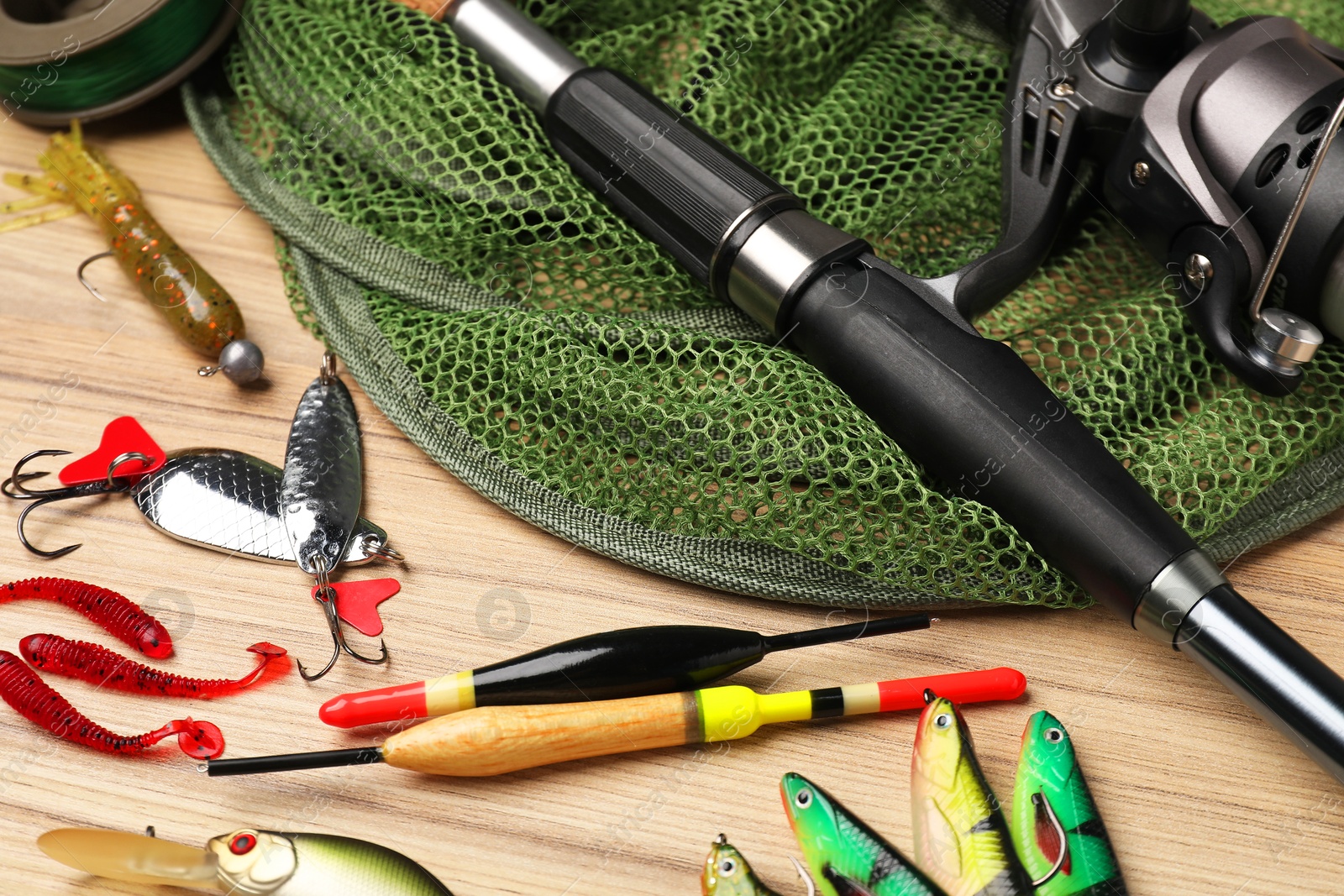 Photo of Fishing rod with spinning reel, baits, net and floats on wooden table