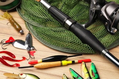 Photo of Fishing rod with spinning reel, baits, net and floats on wooden table