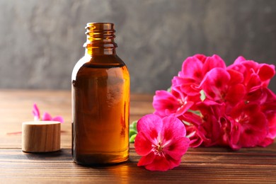 Geranium essential oil in bottle and beautiful flowers on wooden table