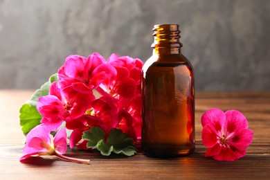 Photo of Geranium essential oil in bottle and beautiful flowers on wooden table