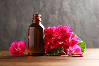 Photo of Geranium essential oil in bottle and beautiful flowers on wooden table