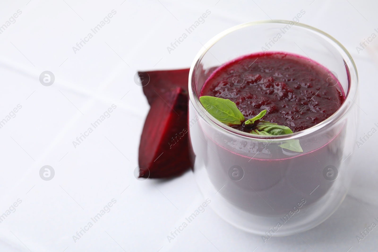 Photo of Fresh beetroot smoothie with mint in glass on white tiled table, closeup. Space for text