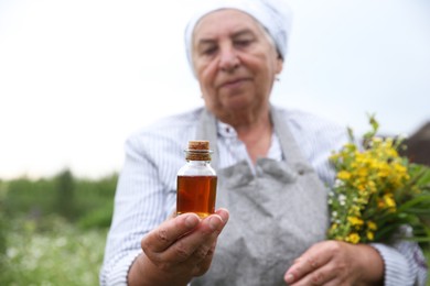 Senior woman with tincture and herbs outdoors, selective focus